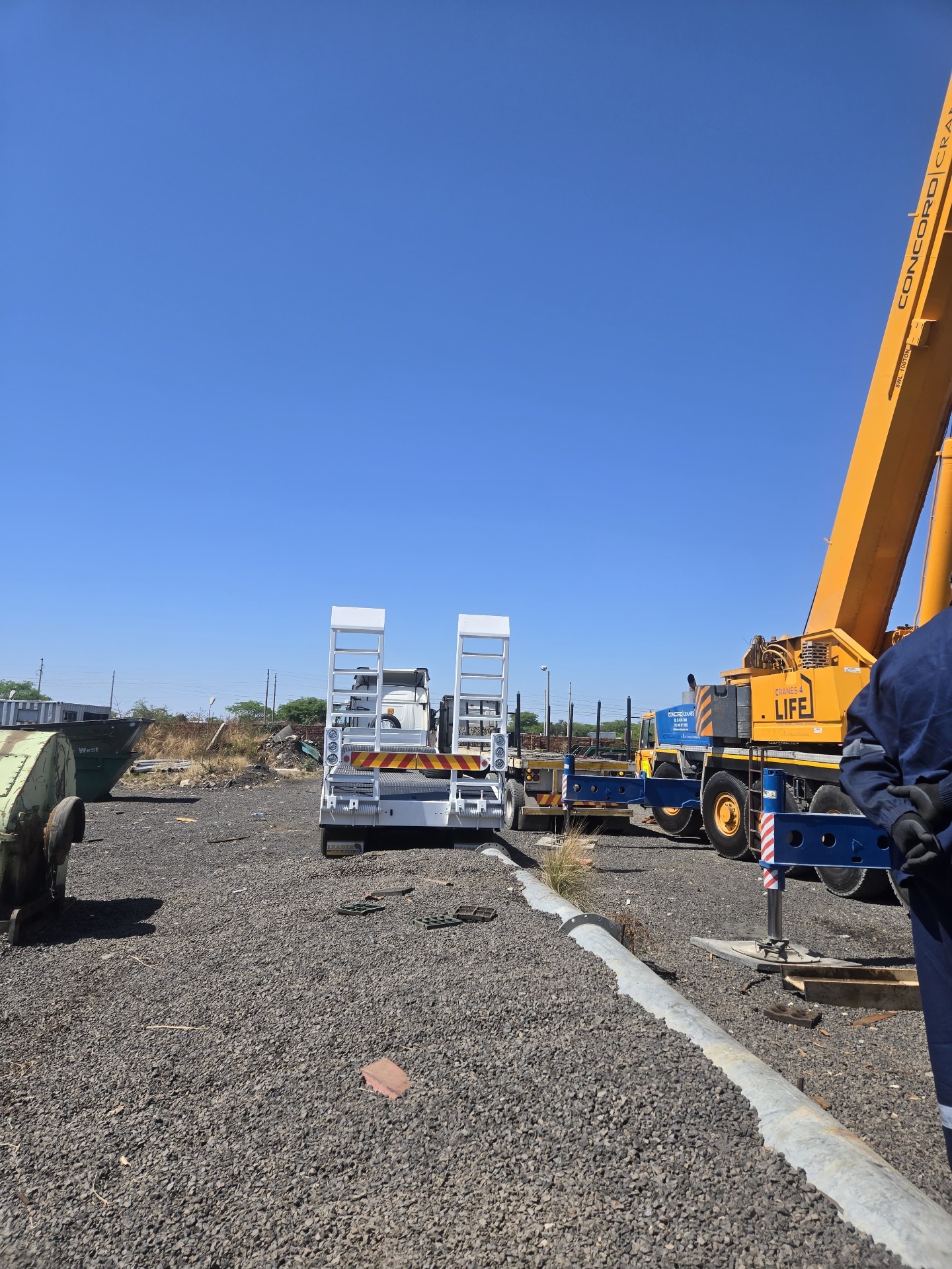 Low-bed trailer and mobile crane at a mining equipment yard