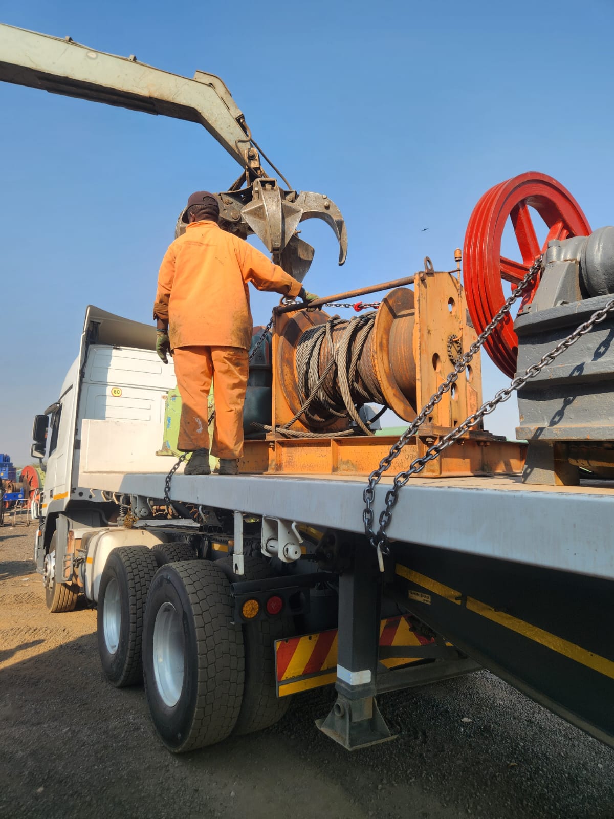 Crane loading a winch and crusher flywheel onto a flatbed