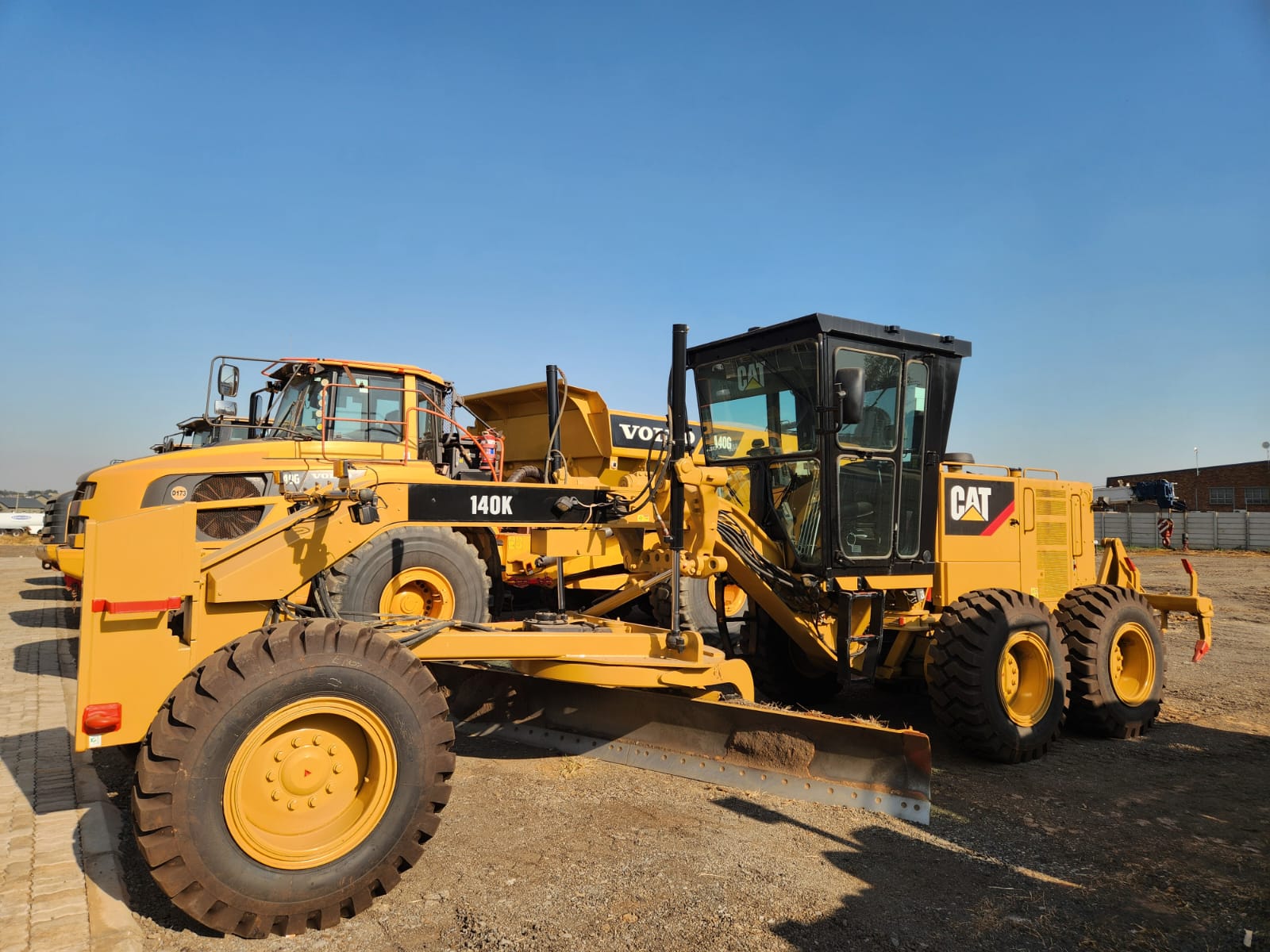 Cat 140K motor grader beside Volvo dump trucks