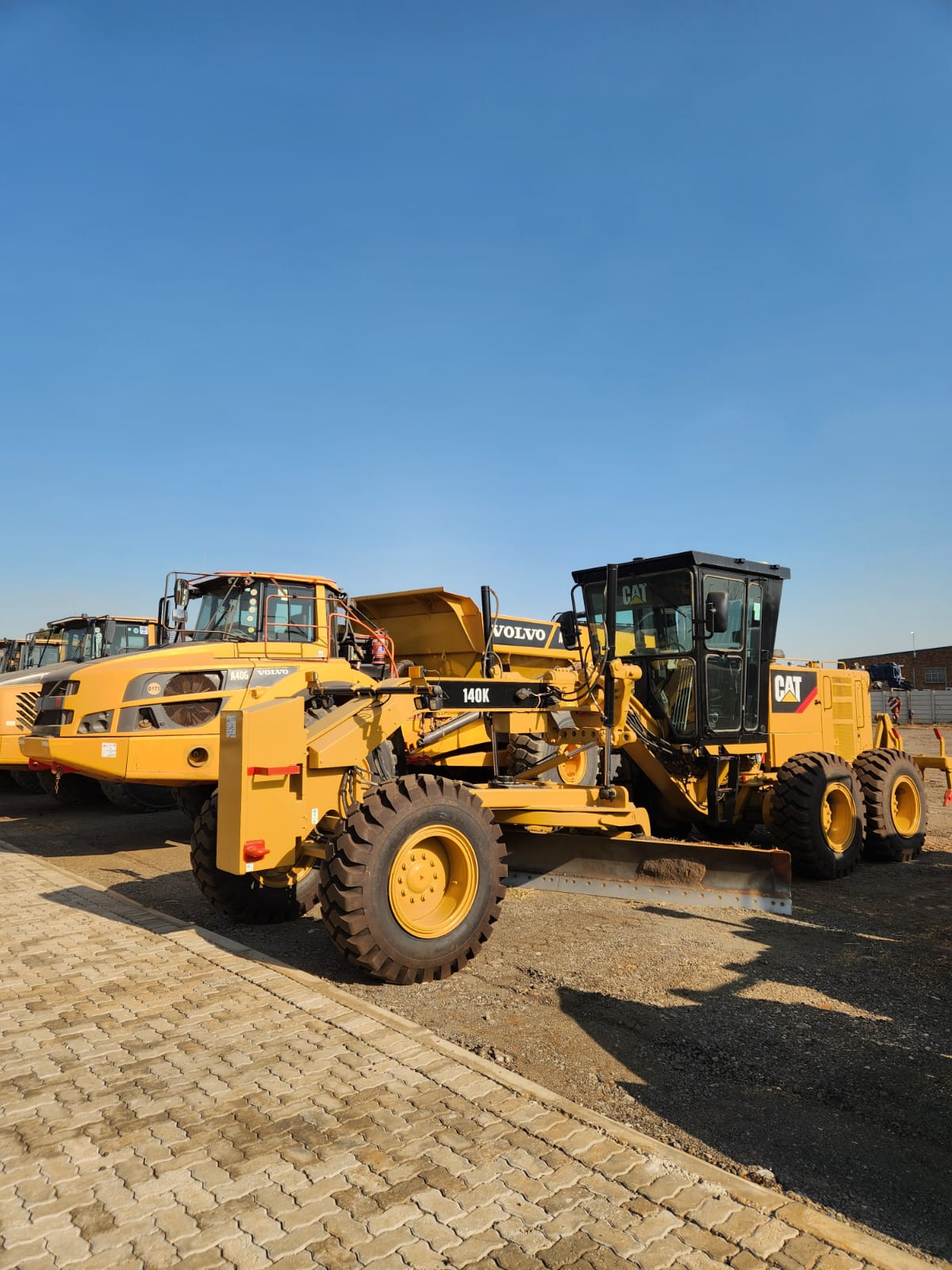 Cat 140K grader and Volvo articulated dump trucks in the yard